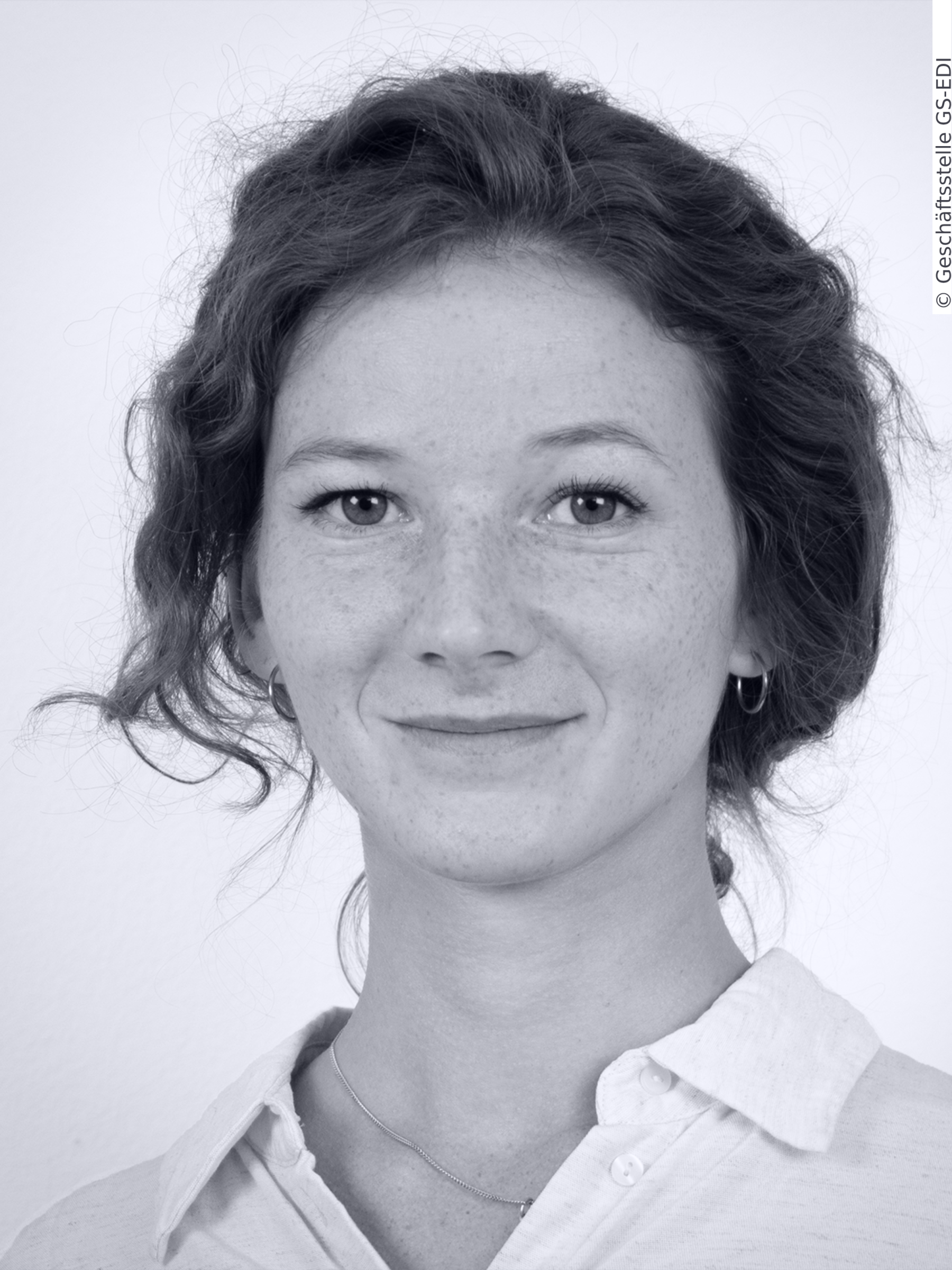 Portrait of Ms Rubina Lanfranchi. Ms Lanfranchi has curly red hair worn in a loose bun. She has green eyes and freckes. She is wearing a white blouse.