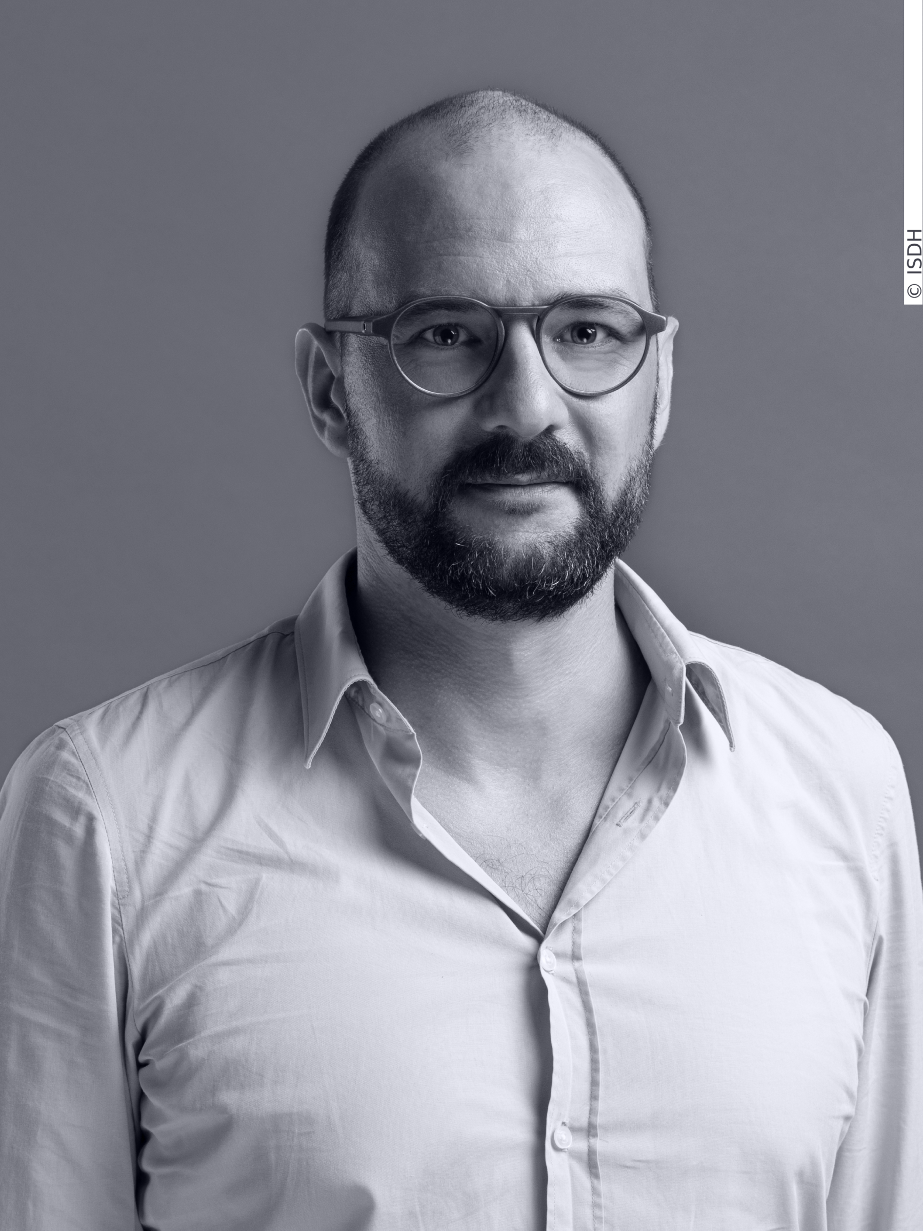 Portrait of Stefan Schlegel. Mr Schlegel wears glasses and a white shirt. He has clear eyes and a dark beard.